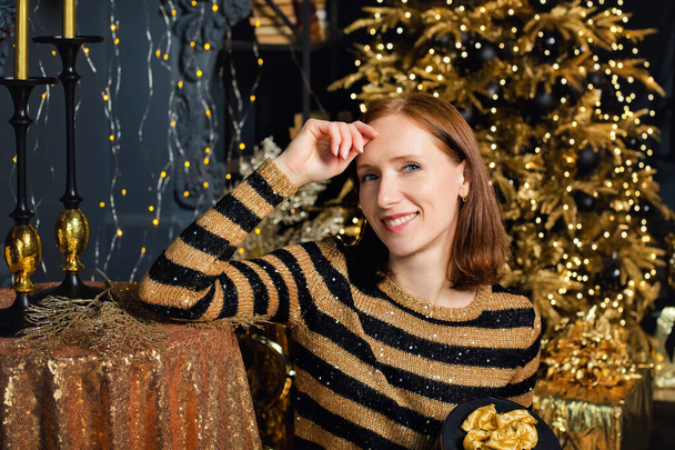 Uma jovem no fundo de uma árvore de Natal com ornamentos dourados. Moda feminina, moda desgaste da noite e acessórios, maquiagem. Feliz Ano Novo. - Foto, Imagem