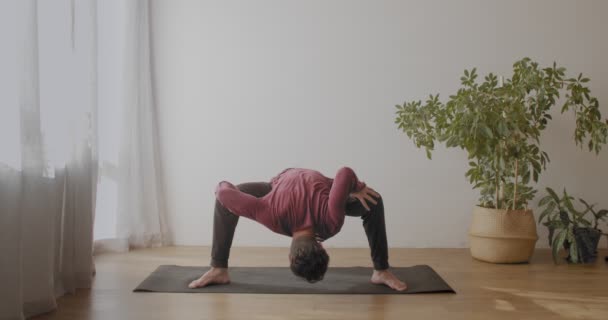 Hombre flexible haciendo yoga en interiores en habitación soleada fondo cámara lenta. Maestro yogui de pie en equilibrio asana pose estiramiento piernas músculos copiar el espacio de texto. Concepto de cuidado corporal estilo de vida saludable - Metraje, vídeo