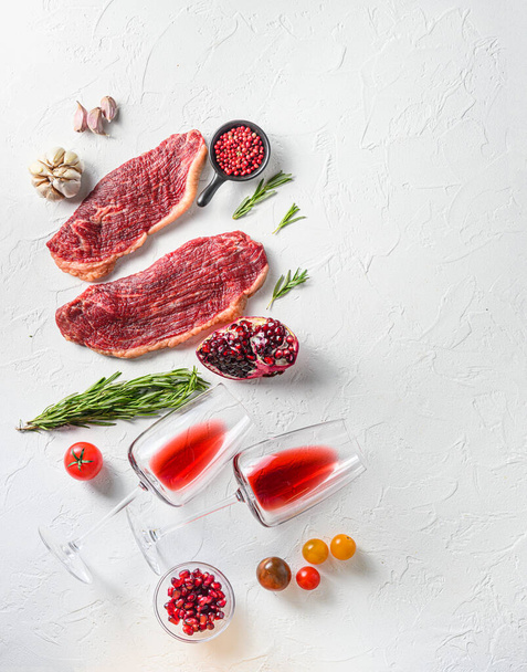Rohes Picanha-Steak mit Gläsern Rotwein, Kräutern und Granatapfel von oben über weißem strukturiertem Hintergrund. Große Größe - Foto, Bild