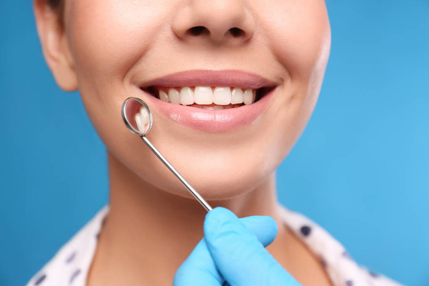 Doctor examining woman's teeth on blue background, closeup. Cosmetic dentistry - Foto, imagen