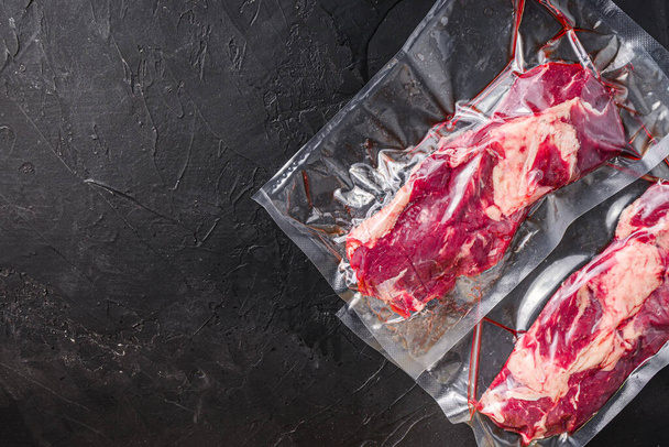 Chuck Nabídky hovězí steak ve vakuově uzavřené tašce na černém texturovaném pozadí horní pohled prostor pro text - Fotografie, Obrázek
