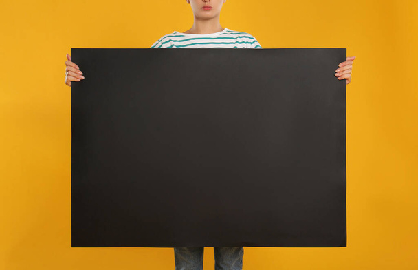 Woman holding black blank poster on yellow background, closeup. Mockup for design - Foto, afbeelding