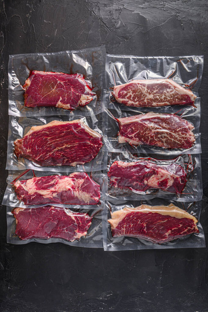 Vákuum csomagolt szerves nyers marhahús alternatív vágások: felső penge, farok, picanha, Chuck roll steak, felett fekete texturált háttér, topview - Fotó, kép