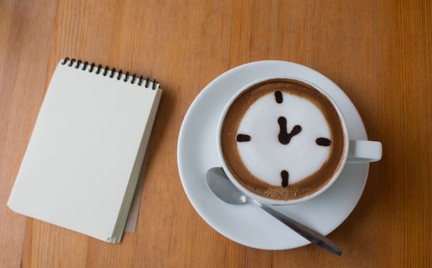Lähikuva A Cup kuuma latte art kahvi piirretty oclock liiketoiminnan käsite puinen pöytä muistiinpanokirja. - Valokuva, kuva