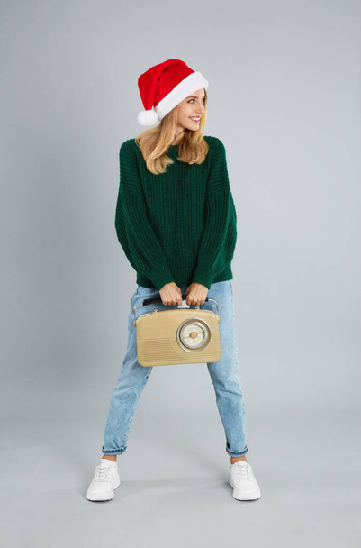 灰色の背景にヴィンテージラジオを持つ幸せな女性。クリスマス音楽 - 写真・画像