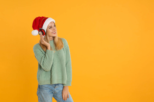 Happy woman with headphones on yellow background, space for text. Christmas music - Fotó, kép