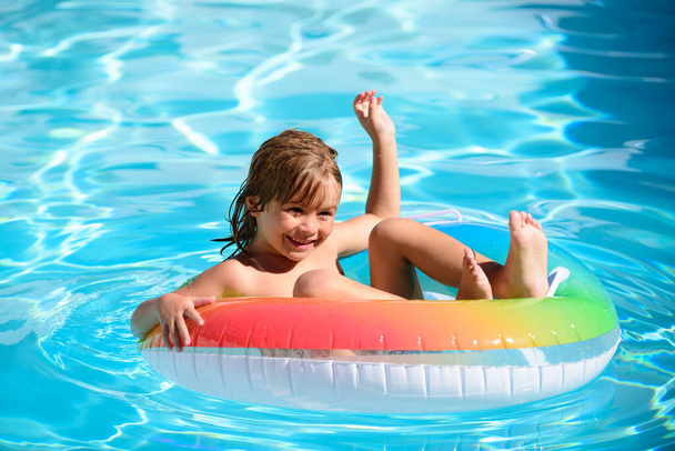 Children in swimming pool. Summer outdoor. Happy kid playing with colorful swim ring in swimming pool. Child water toys. Children play in tropical resort. Family beach vacation. - Fotó, kép