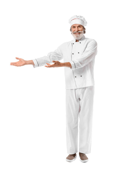 Ältere männliche Koch zeigt etwas auf weißem Hintergrund - Foto, Bild