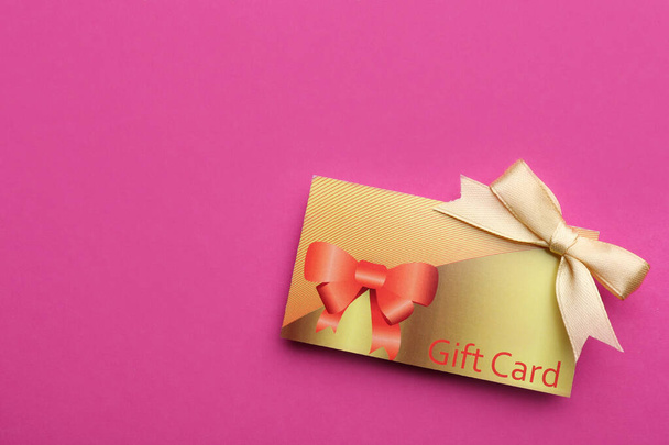 Gift card with bow on pink background, top view. Space for text - 写真・画像