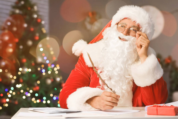 Santa Claus making list of gifts at table - Photo, Image