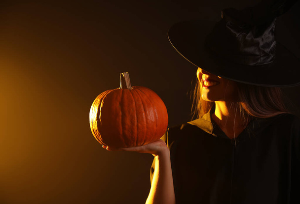 Young woman wearing witch costume with pumpkin on dark background. Halloween party - Foto, Imagem