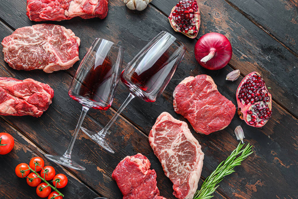 Carne de carne bifes conceito de quadro, com diferentes cortes de bife e dois copos de vinho no quadro na vista lateral da mesa de madeira velha escura - Foto, Imagem