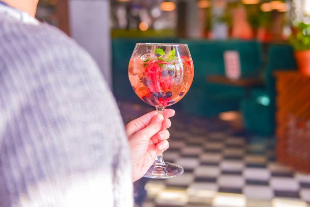 Raspberry Cocktail with ice and berry. Refreshing cocktail with berries inside. Delicious alcohol drink served in a tall wine glass in womans hand. Blurred restaurant background. - Foto, afbeelding