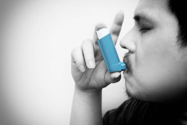 Hombre graso asiático usando un inhalador de cartucho presurizado faringe extendida, broncodilatador. fondo blanco. Tono blanco y negro excepto el broncodilatador - Foto, Imagen