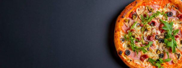 Hot tasty delicious rustic homemade american pizza over black background. Flat lay, top view. Traditional Italian cuisine concept. Pizza with salami, mushrooms, olives. Copy space banner. - Foto, imagen