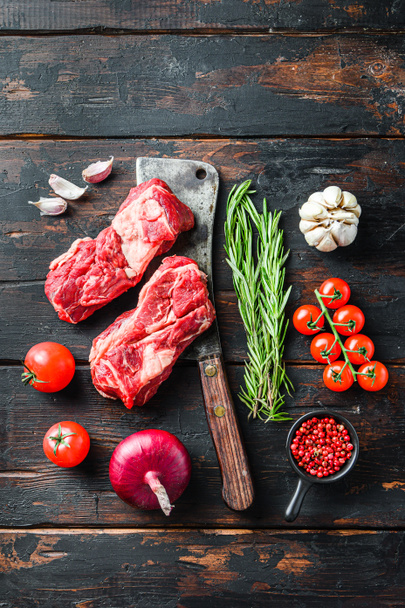 Organický syrový hovězí steak s rozmarýnovým červeným oninem, česnekovou paprikou a rajčaty na starém tmavém dřevěném stole. Horní pohled - Fotografie, Obrázek