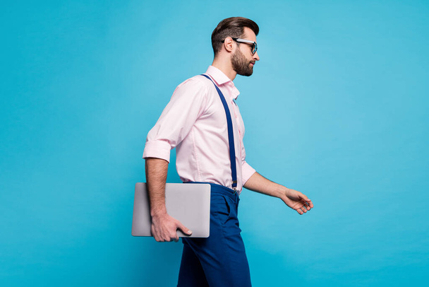 Profile photo of handsome confident business man hold computer walk meeting office successful young worker wear specs shirt suspenders pants isolated blue color background - Foto, Imagen