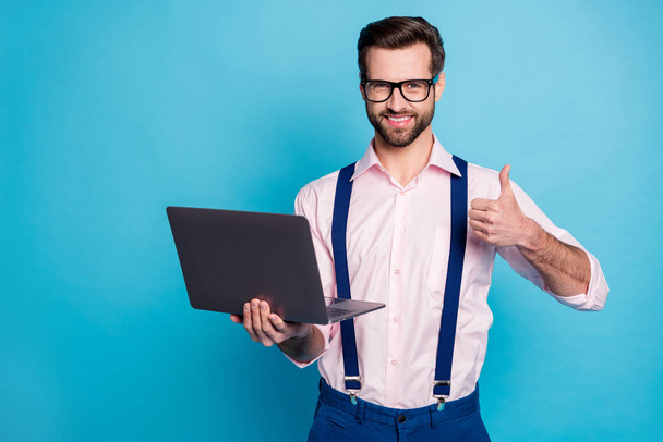 Photo of handsome business man trend outfit guy working computer read report stay home quarantine raise thumb up wear specs pink shirt suspenders pants isolated blue color background - Foto, afbeelding