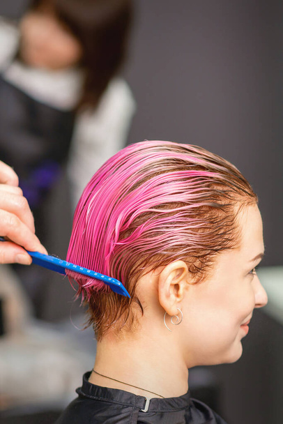 Νεαρή γυναίκα που λαμβάνει θεραπεία μαλλιών μετά από ροζ χρώμα με το χέρι του ανδρικού κομμωτηρίου στο κομμωτήριο - Φωτογραφία, εικόνα