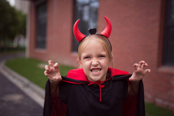 公園で赤い角を持つ悪魔の衣装の少女。ハッピーハロウィンのコンセプト - 写真・画像