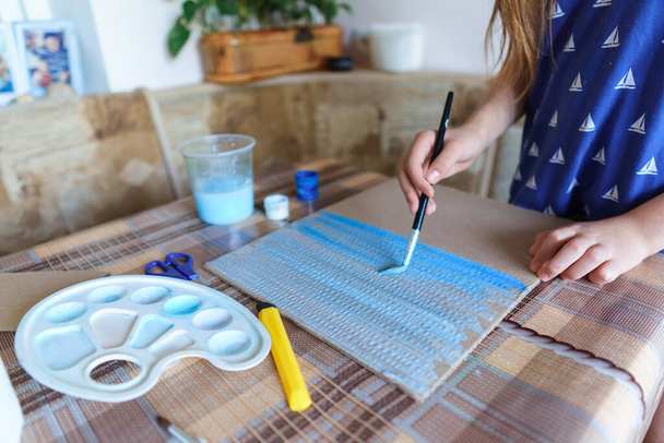 a menina desenha papelão guache azul, faz um fundo, senta-se na cozinha da casa - Foto, Imagem