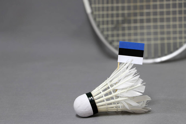 Mini bandera de Estonia se pega en el volante blanco en el fondo gris y fuera de foco raqueta de bádminton. Concepto de deporte de bádminton.  - Foto, imagen