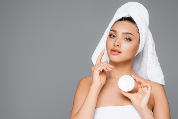 donna con asciugamano sulla testa applicando crema cosmetica sul viso isolato su grigio - Foto, immagini
