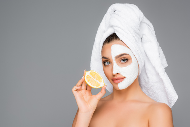 woman with towel on head and clay mask on face holding lemon isolated on grey - Photo, Image