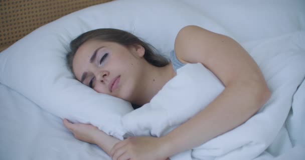 Young woman wakes up in bed in the morning smiling raises her hands - Footage, Video
