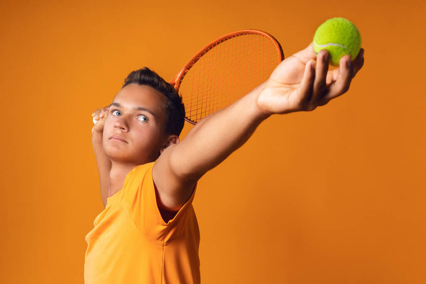 Studio shot of a young tennis player holding racket against orange background - Foto, immagini