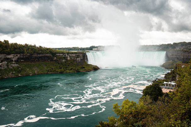 Widok na wodospad Niagara z Kanady. Chmury, ale słoneczna pogoda, zielona woda. - Zdjęcie, obraz