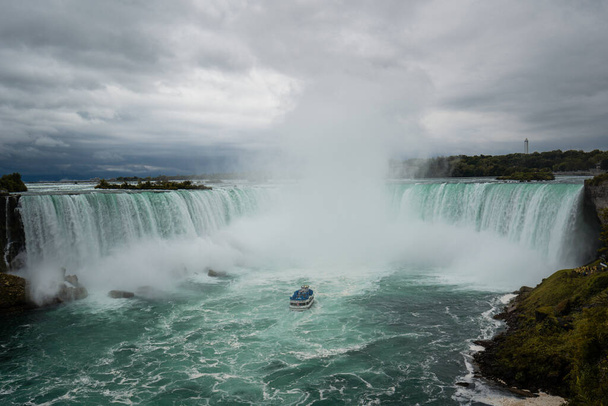Widok na wodospad Niagara z Kanady. Chmury, ale słoneczna pogoda, zielona woda. - Zdjęcie, obraz