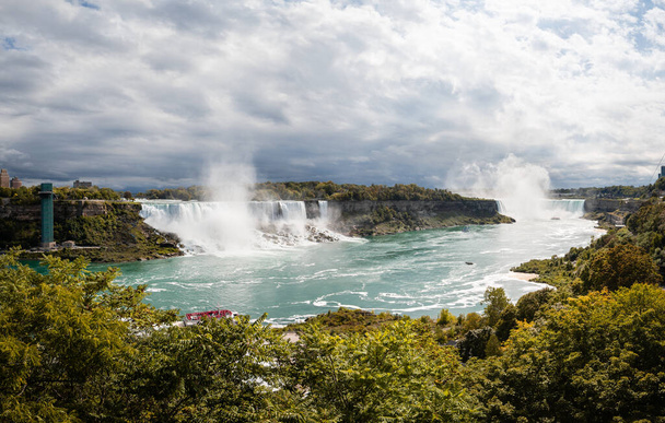 Panoramiczny widok na wodospad Niagara. Chmury, ale słoneczna pogoda, łodzie na zielonej wodzie. - Zdjęcie, obraz