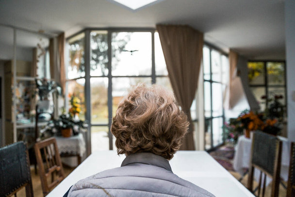 Grootmoeder in haar huis met grote ramen op zoek in haar tuin - Foto, afbeelding