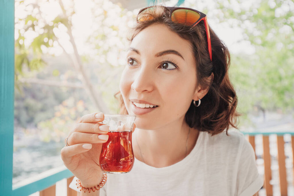 Happy middle Eastern woman drinks traditional Turkish tea on the veranda or terrace of an outdoor restaurant - Foto, Imagen