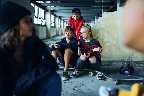 Grupo de adolescentes pandilla sentados en el interior de un edificio abandonado, utilizando teléfonos inteligentes. - Foto, Imagen