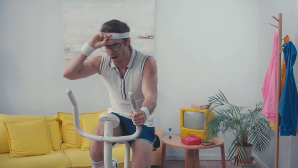 Sportowiec w okularach trening na rowerze treningowym w salonie - Materiał filmowy, wideo