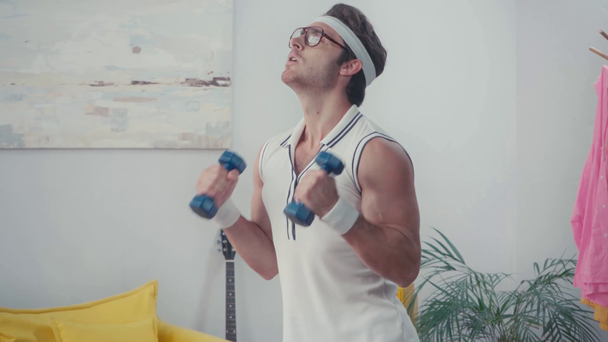 Funny sportsman lifting dumbbells in living room, retro sport concept - Footage, Video