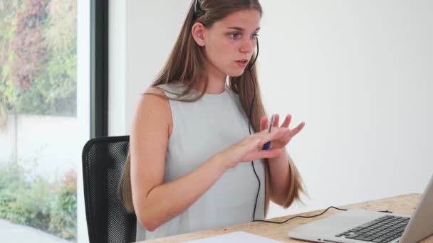 egy női munkavállaló távoli beszélgetést folytat, és megállapodik egy laptop és egy mikrofonnal rendelkező fülhallgató használatával - Felvétel, videó