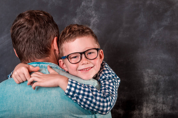 Kleiner Sohn umarmt seinen Vater in der Nähe von wal. Glücklicher Vater und kleiner Junge an Händen. Schulkind mit Brille. Vatertag - Foto, Bild