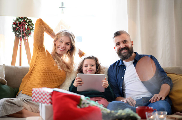 Couple with small daughter indoors at home at Christmas, having video call. - Foto, Imagem