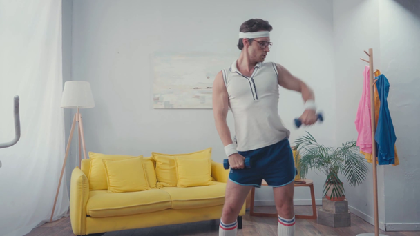 スポーツマンはダンベルを持ち上げリビングルームで腰を振っている間 - 映像、動画