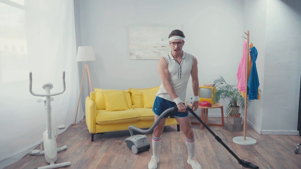 Energetischer Sportler wackelt mit den Hüften, während er sein Wohnzimmer staubsaugt - Filmmaterial, Video