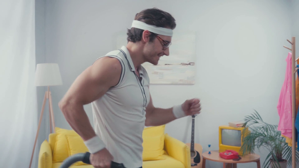 Энергичный спортсмен ритмично танцует с пылесосом в гостиной - Кадры, видео