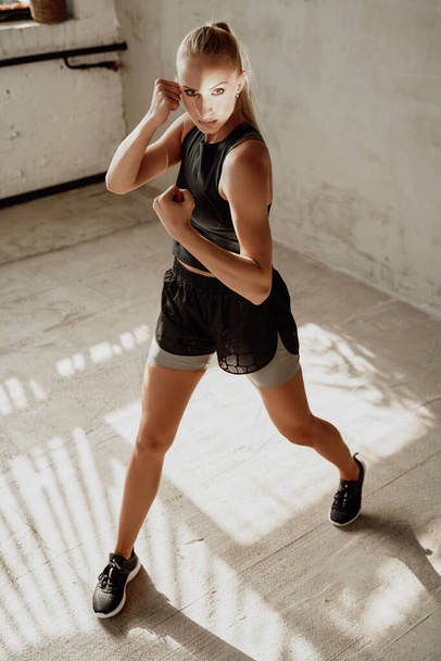 Rubia deportiva permaneciendo en pose de lucha en la habitación del estudio blanco - Foto, Imagen