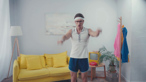 Front view of funny sportsman lifting arms in living room, retro sport concept - Footage, Video