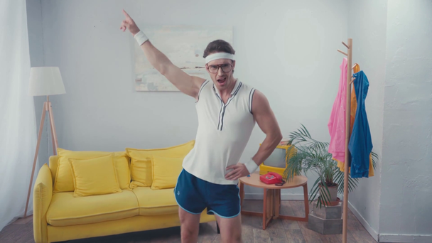 Frontansicht des energischen Sportlers mit der Hand auf der Hüfte, der im Wohnzimmer tanzt - Filmmaterial, Video