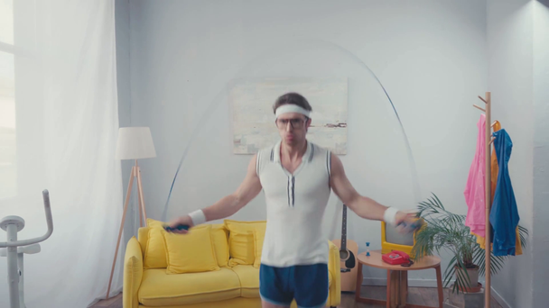 Energetic sportsman jump roping in living room, retro sport concept - Footage, Video