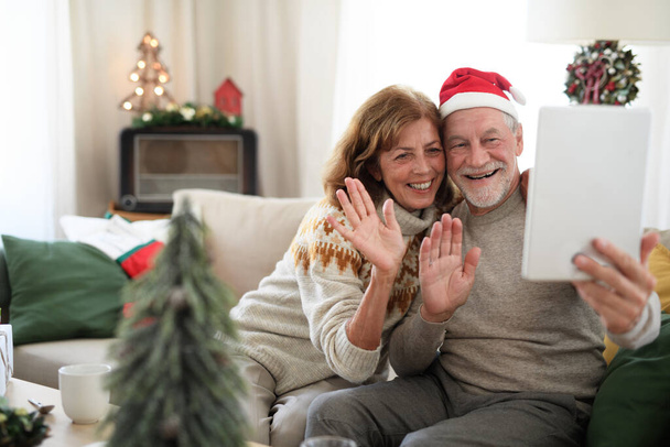 Vue de face du couple de personnes âgées à l'intérieur à la maison à Noël, en prenant selfie. - Photo, image