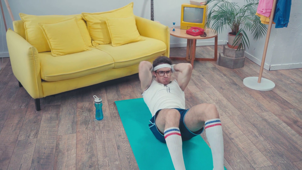 Deportista haciendo abdominales en la alfombra de fitness en la sala de estar, concepto de deporte retro - Metraje, vídeo